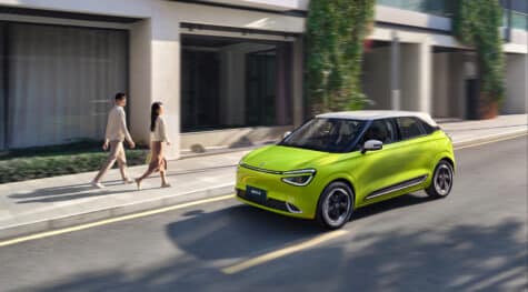 Kollane linnaelektriautomobil Dongfeng Box valge katusega sõidab linnas, vaade eest ja küljelt